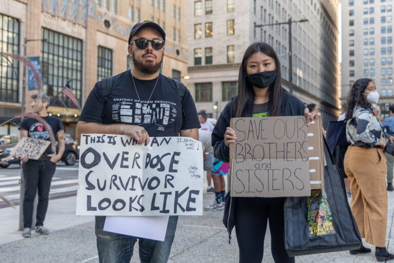 Protesters hold signs advocating for supervised injection sites.