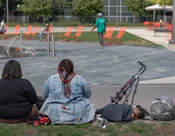 2 woman with a young child sitting on the ground in the park.