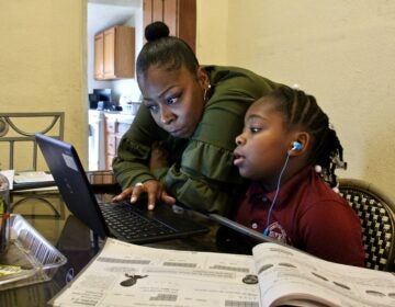 Yolanda Biggers helps her daughter, Zyiah Satterwhite, 7, find her assignment.  After the coronavirus pandemic hit, Biggers gave up her shifts as a part-time nurse to focus all of her attention on Zyiah and her two older sisters as they adapted to virtual schooling. (Emma Lee/WHYY)