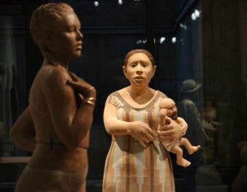 A figure holding a man baby gazes towards another sculpted figure.