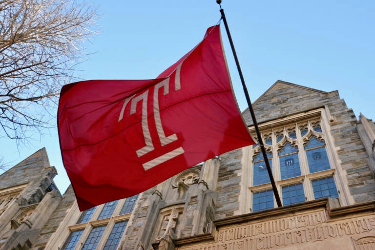 A view of a Temple flag from below, flying outside of a university building.