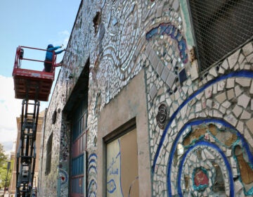 Andrew Jeffries and Stacey Holder stand on a lift, chiseling pieces from a mural on a building.