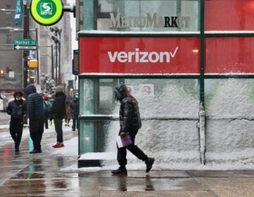 A pedestrian passes by a Verizon store with windows coated in frost and snow.