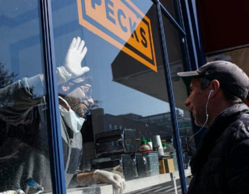 Peck's Food owner Theodore Peck touches hands with a customer through window glass while closing his storefront due to the coronavirus outbreak, Wednesday, March 18, 2020, (AP Photo/John Minchillo)