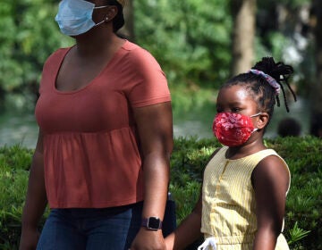 A child and her mother wear face masks while walking through a park