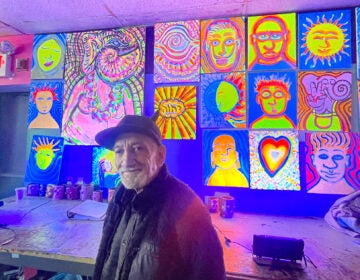 Ken Segal standing in front of a wall of brightly colored artworks