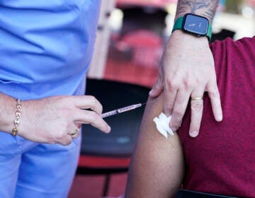 A close-up of a nurse injecting a syringe, filled with a vaccine, into a patient's arm.