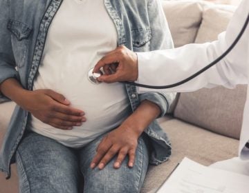 A doctor holds a stethoscope on a pregnant person's belly.