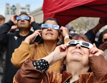 Three people are seen holding up eclipse glasses as the eclipse streaks across Philadelphia