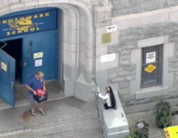 A person leaving out of the front door of Southwark Elementary with a box of possessions in hand.