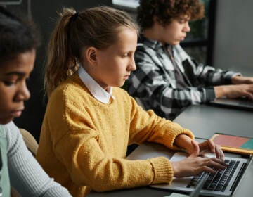 Three students seated at a table look at laptops.