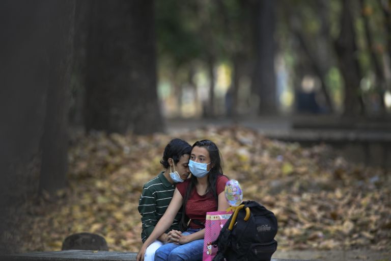 A couple wearing masks curb the spread of the new coronavirus sit together at a public park in on Sunday, Feb. 14, 2021. (AP Photo/Matias Delacroix)