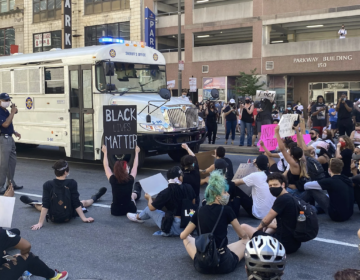 Protesters sitting in the street, blocking a prison transport bus