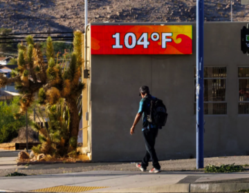 A man walking outside with a digital sign showing temperature is 104 degrees